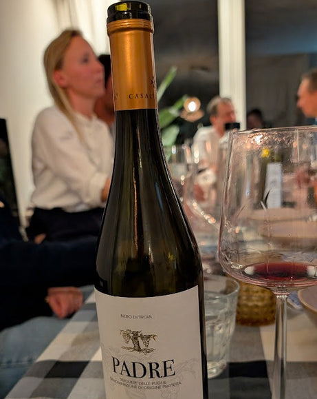 Wine bottle labeled 'Padre' on a checkered tablecloth with people in the background
